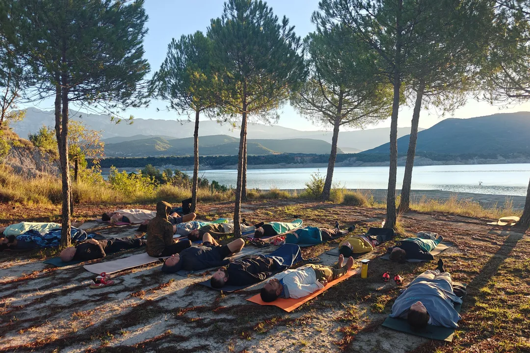 Gruppe liegt bei einer geführten Atemsession auf Matten unter Bäumen an einem Bergsee