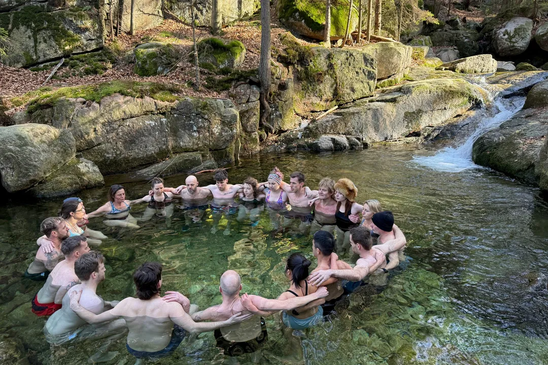 Gruppe steht beim Kältetraining im Kreis in einem natürlichen Gebirgsbach zwischen Felsen