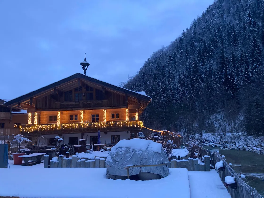 Haus Anni im Winter, beleuchtet in der Dämmerung, dahinter verschneiter Bergwald