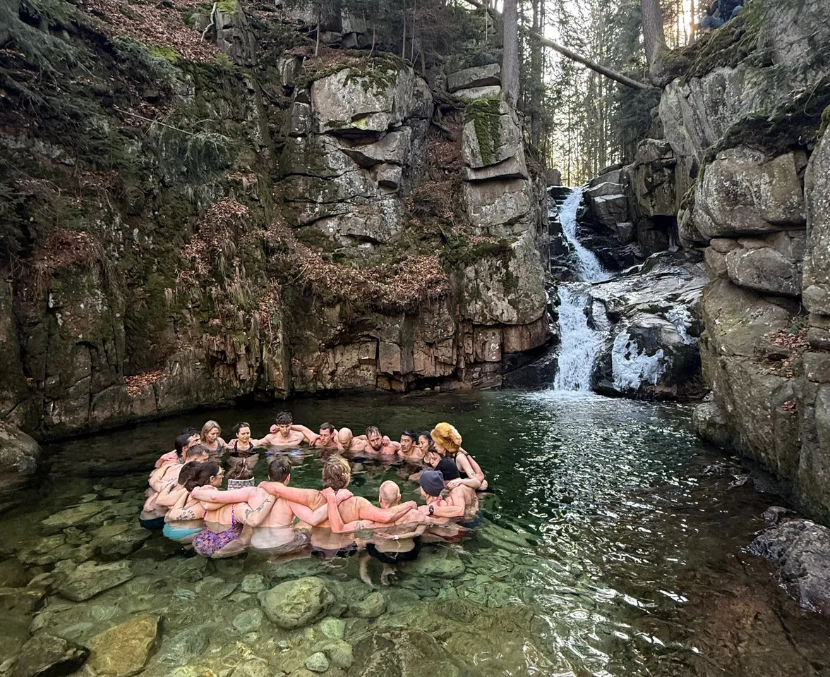 Gruppe steht im Kreis in einem Gebirgsbach unterhalb eines Wasserfalls