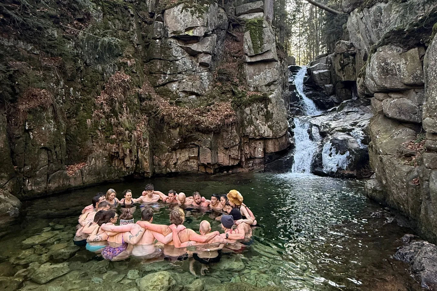 Gruppe im Kreis beim Eisbaden in einem Bergbach unterhalb eines Wasserfalls – Wim Hof Method Winter Travel in Polen