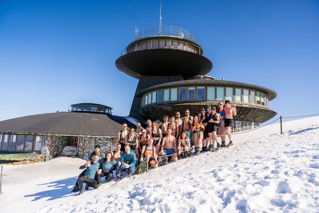 Gruppe in Badekleidung im Schnee vor dem Gipfelgebäude der Schneekoppe unter blauem Himmel